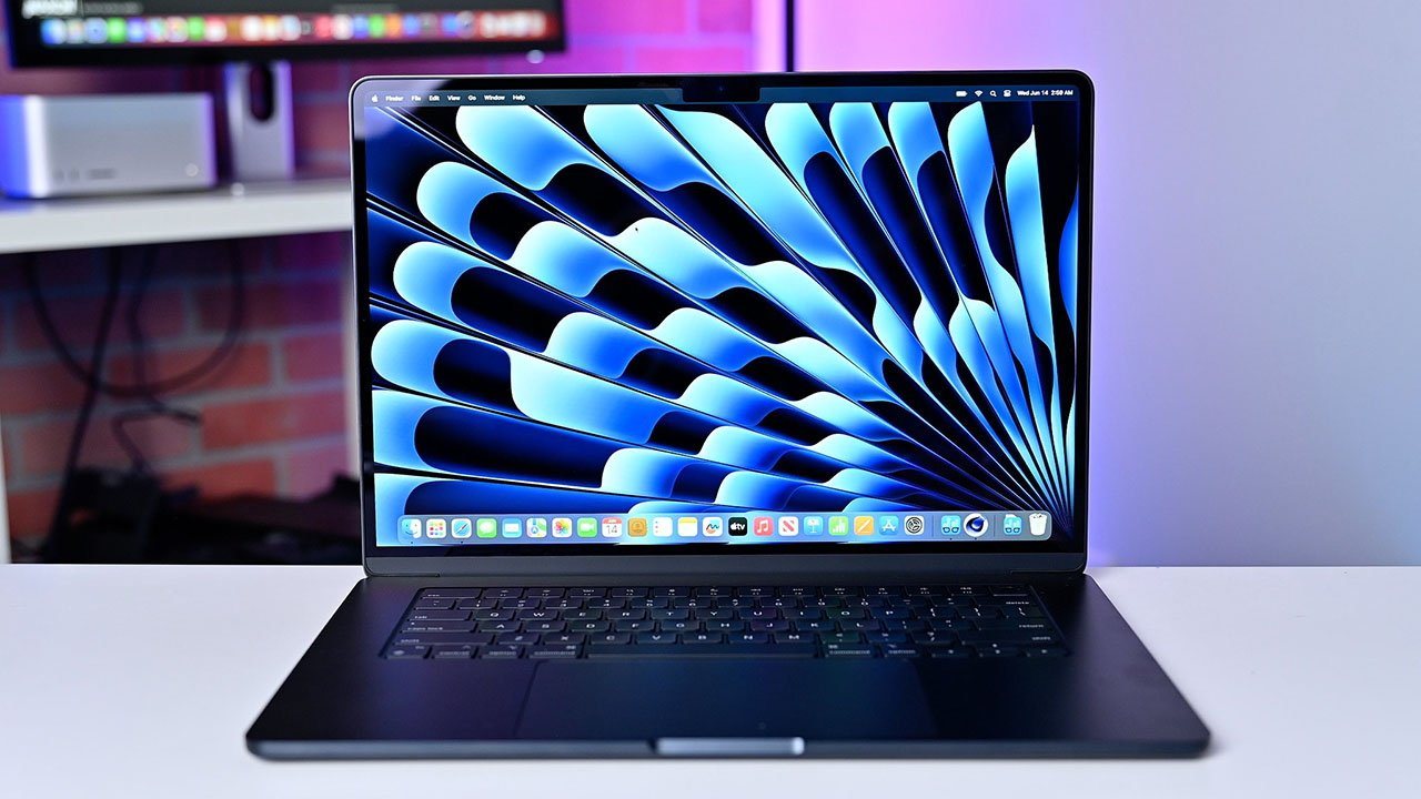 Půlnoční MacBook Air 15palcový notebook na stole s modrou abstraktní tapetou s rozostřeným barevným pozadím.