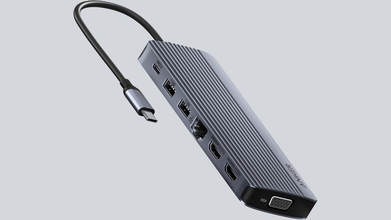 Obdélníkový rozbočovač USB-C s několika porty, včetně USB, Ethernetu, HDMI, VGA a portu pro napájení.  Připojený kabel vyčnívající z horní části.