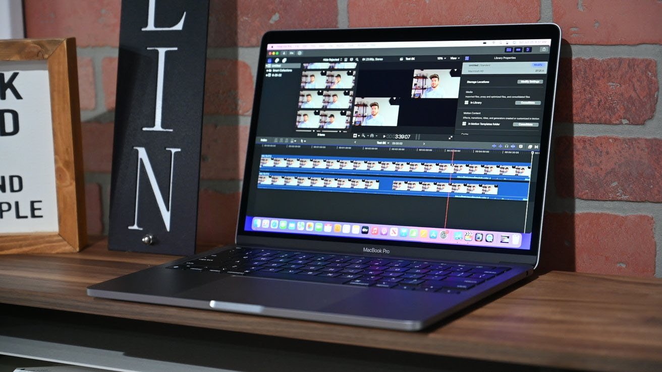 M3 MacBook Pro na dřevěném stole se softwarem pro úpravu videa na pozadí cihlové zdi.