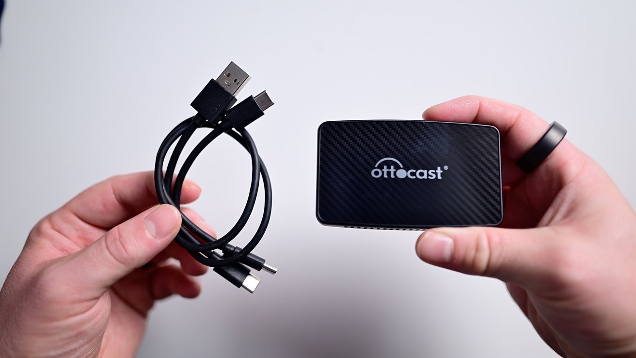 Ruce držící stočený kabel USB a malé černé obdélníkové zařízení se slovem „Ottocast“ na něm.