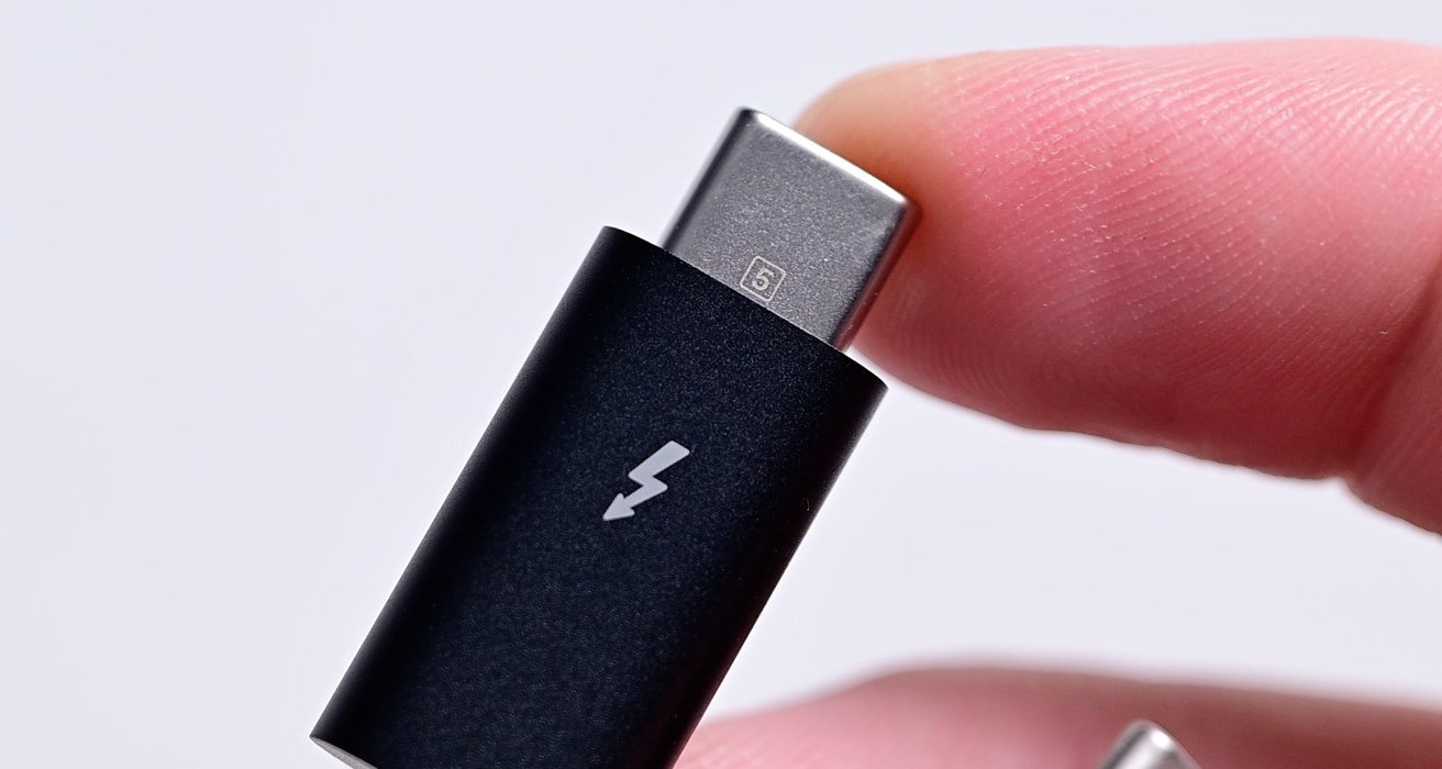 Detail prstů držících kabel USB-C se symbolem blesku na černém konektoru.